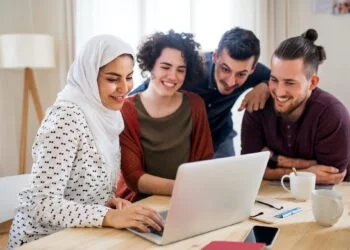A multi-ethnic group of young friends with laptop indoors, house sharing concept