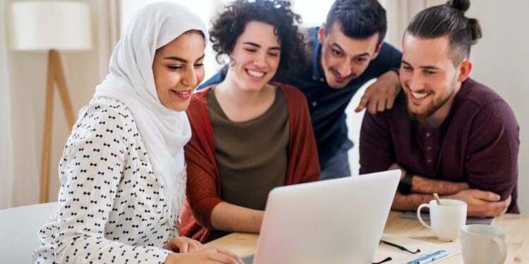 A multi-ethnic group of young friends with laptop indoors, house sharing concept