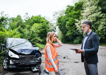 An insurance agent talking to a woman driver by the car on the road after an accident.
