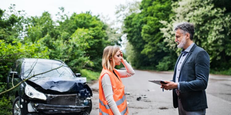 An insurance agent talking to a woman driver by the car on the road after an accident.