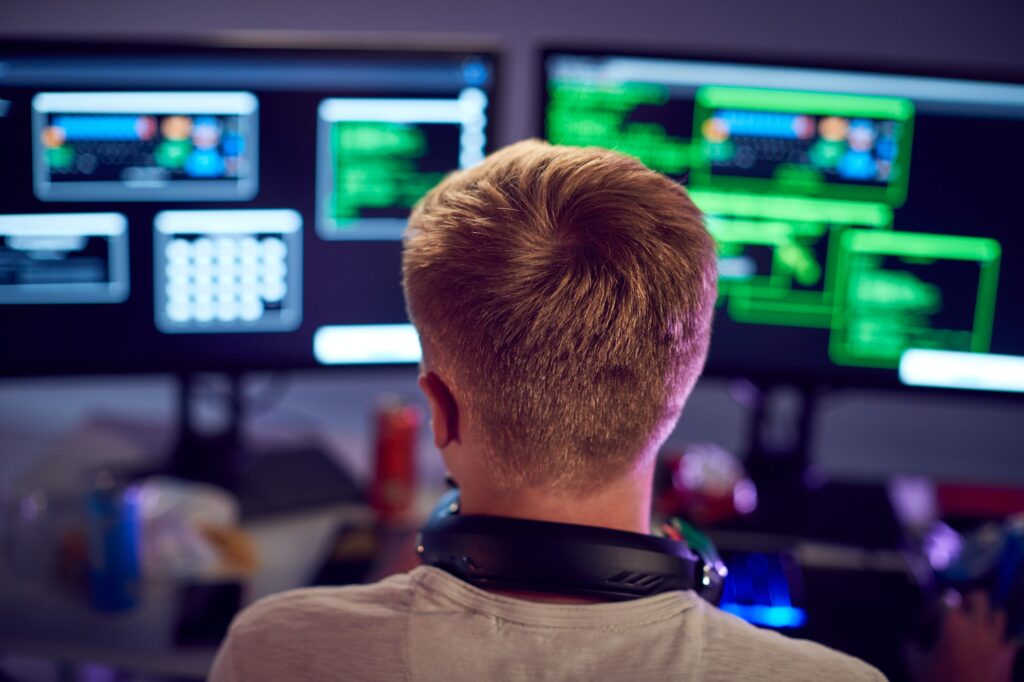 Male Teenage Hacker Sitting In Front Of Computer Screens Bypassing Cyber Security