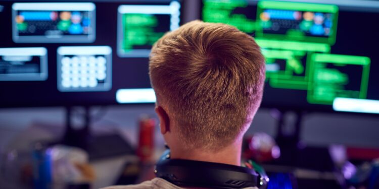 Male Teenage Hacker Sitting In Front Of Computer Screens Bypassing Cyber Security