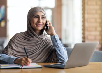 Muslim woman freelancer talking to client on phone, taking notes