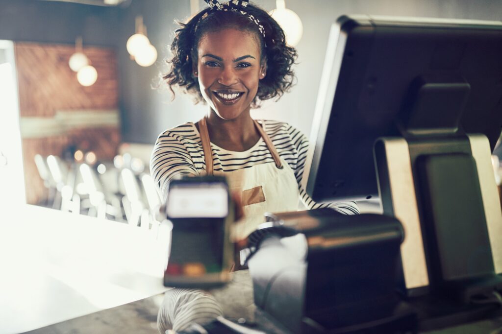 Smiling young bistro waitress holding an electronic card payment machine