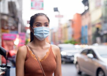 Young Asian tourist woman thinking with mask for protection from corona virus outbreak and pollution