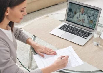 Young woman filling in health insurance form and watching online video