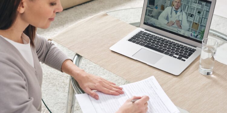 Young woman filling in health insurance form and watching online video