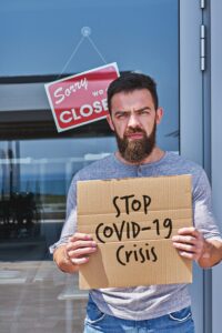 Unemployed guy with sign STOP COVID-19 CRISIS near closed door office or cafe - The present Global challenges impacting the future